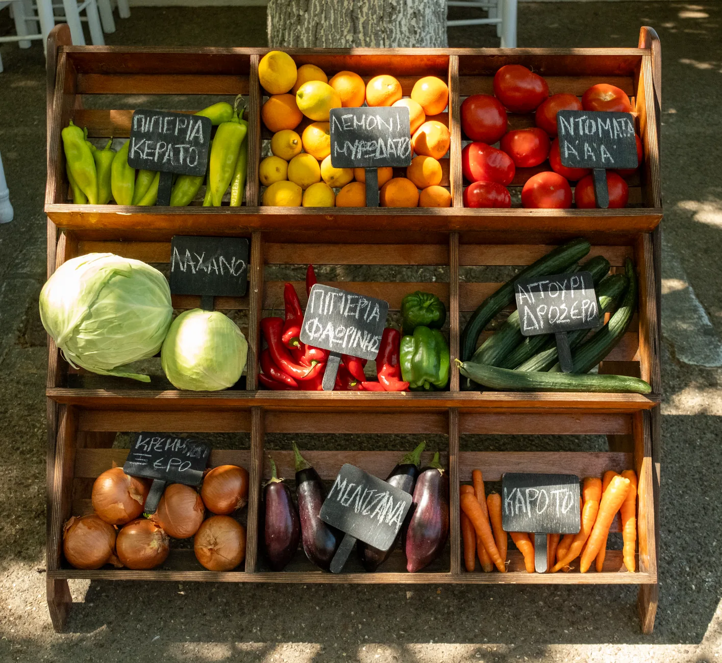 Étal de marché avec légumes et agrumes en caisses de bois, étiquettes de prix en grec