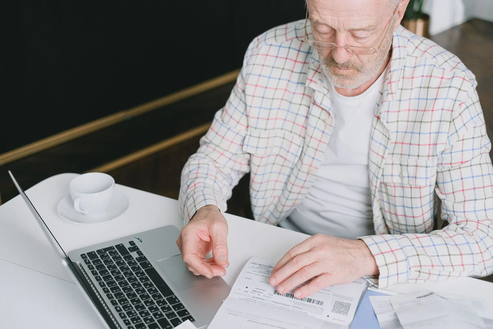 Retraité examinant ses documents administratifs devant son ordinateur portable